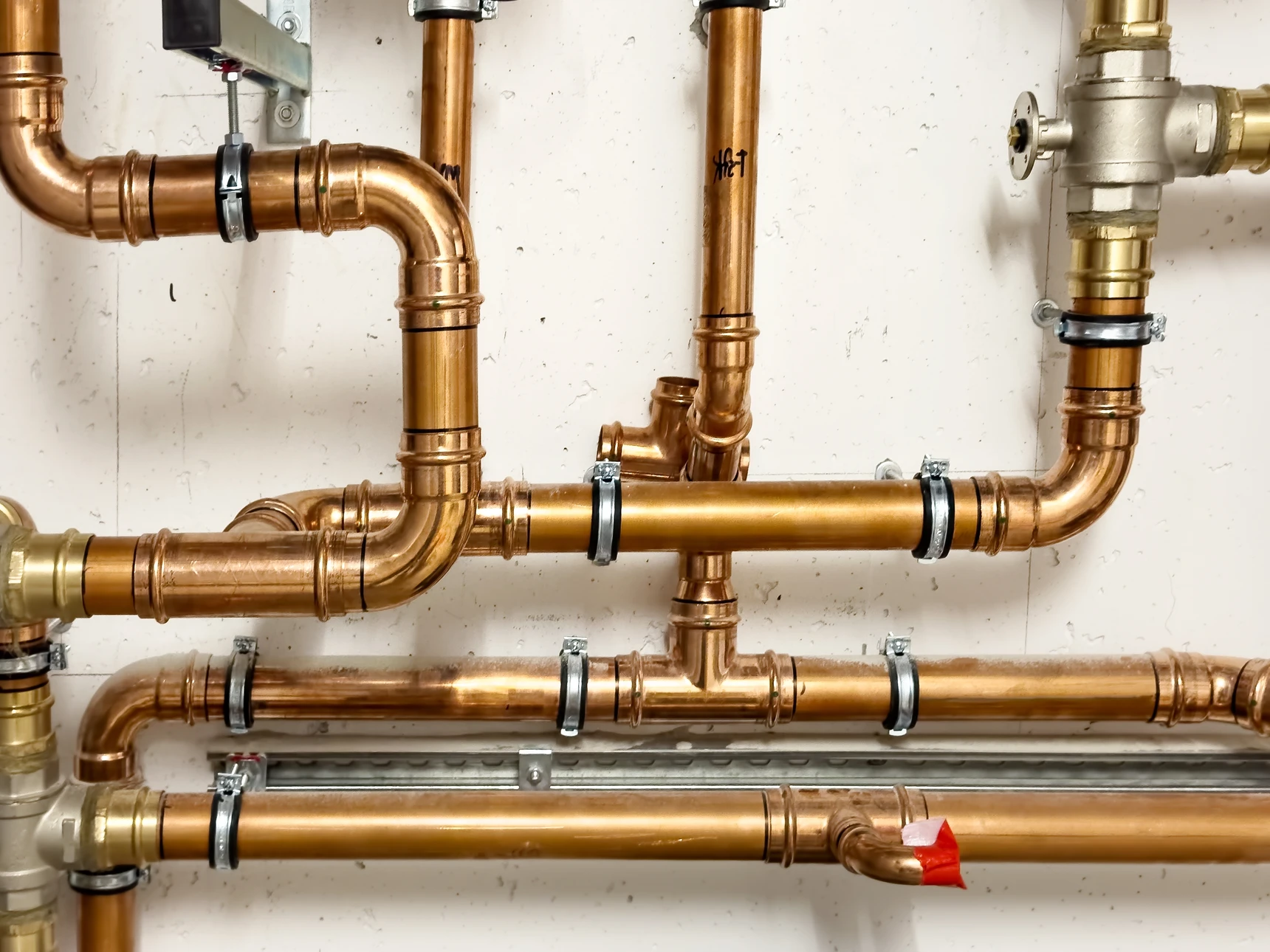 Plombier en uniforme rouge travaillant dans une chaufferie résidentielle, utilisant un outil de détection sur des canalisations en cuivre