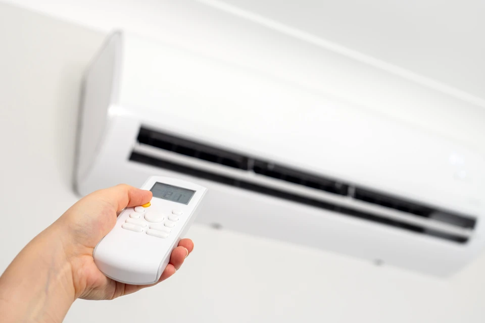 Technicien en uniforme bleu et casque blanc installant une unité de climatisation murale intérieure dans une pièce aux murs blancs
